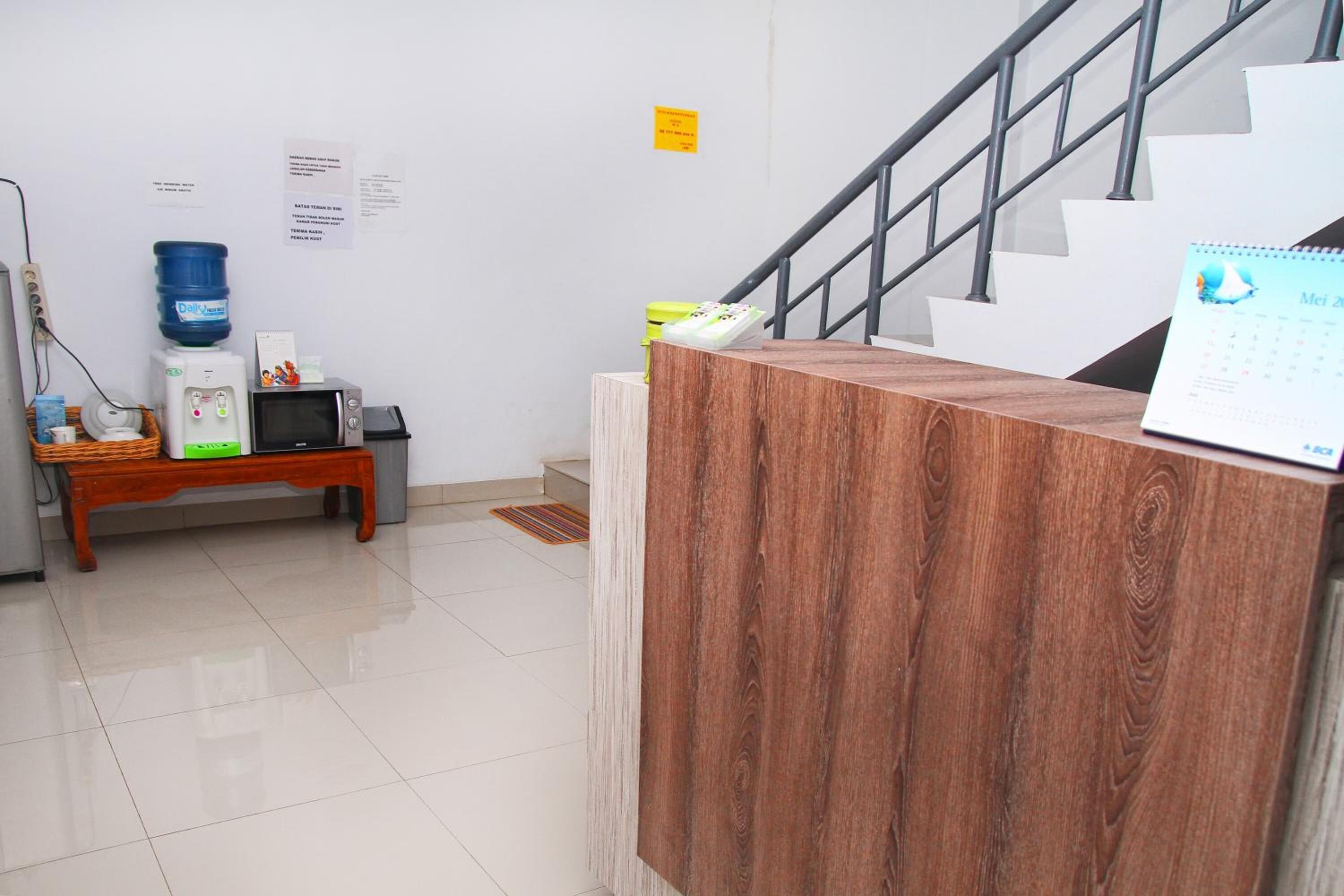 Un espace d’accueil comprenant un comptoir de réception en bois, un distributeur d’eau, un four à micro-ondes et un calendrier accroché au mur.