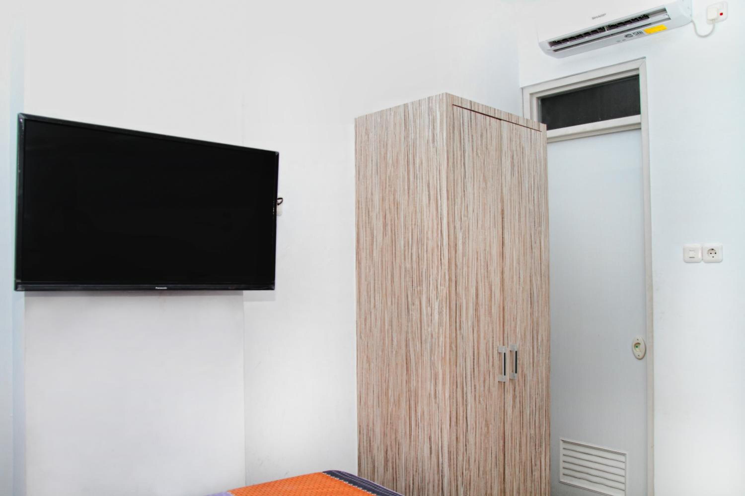 A room with a flat-screen TV mounted on the wall, a wooden wardrobe, and a door with a window.