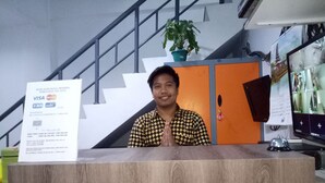 A reception desk with a wooden finish, a potted plant, and a calendar on the wall. - Hotel Syariah Mama Cengkareng (Jakarta)