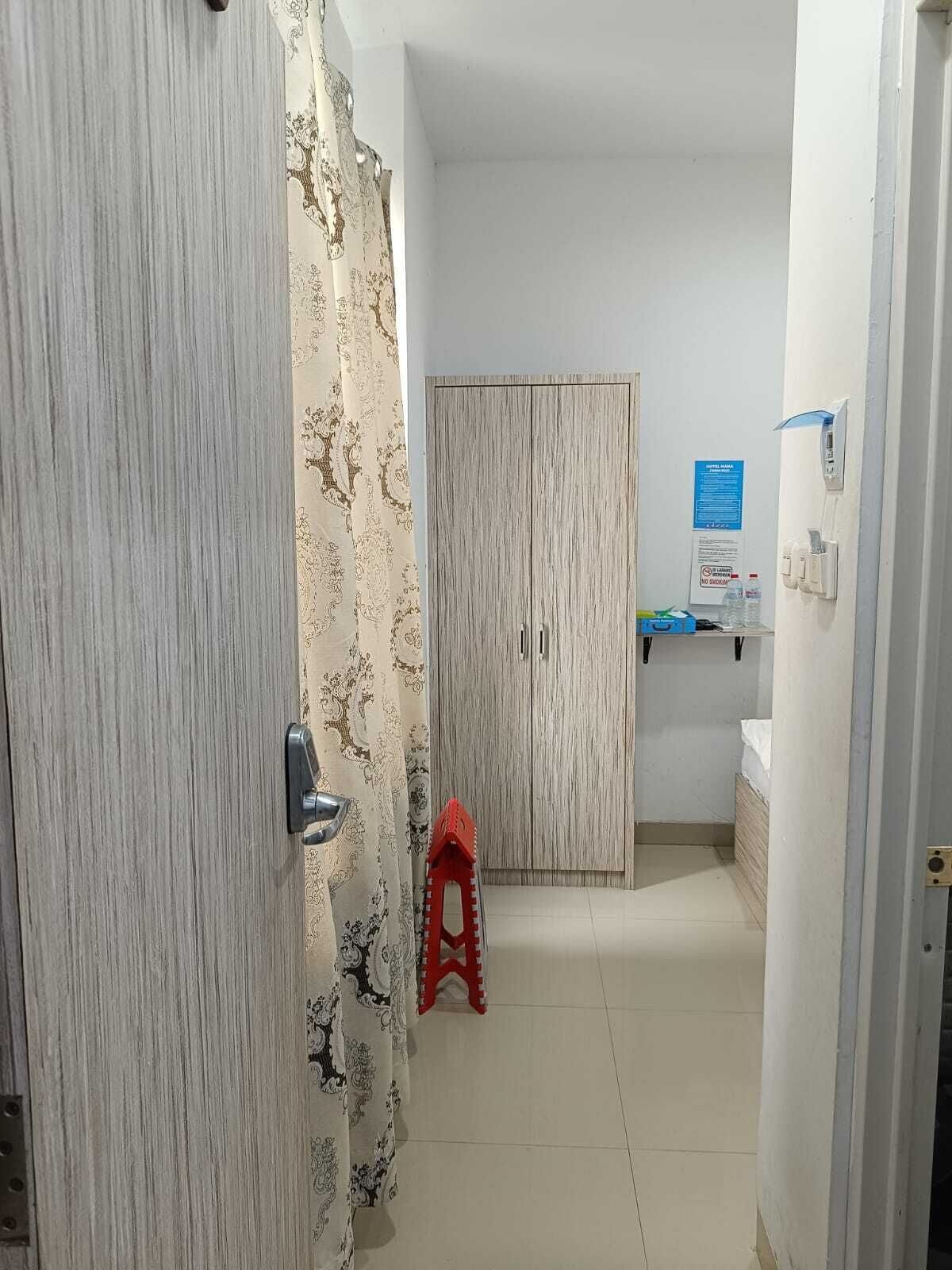 A narrow hallway with a patterned door, a wooden wardrobe, a small red stool, and a blue sign on the wall.