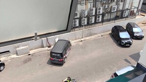 A street view with parked cars, a motorcycle, and a building with multiple air conditioning units. - Hotel Syariah Mama Cengkareng (Jakarta)