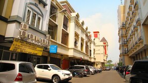 A street with multi-story buildings, parked cars, and a signboard for a business. - Hotel Syariah Mama Cengkareng (Jakarta)