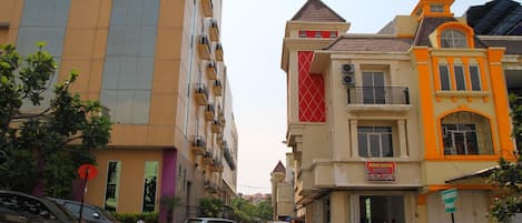 A street view with multi-story buildings, parked cars, and a few pedestrians.