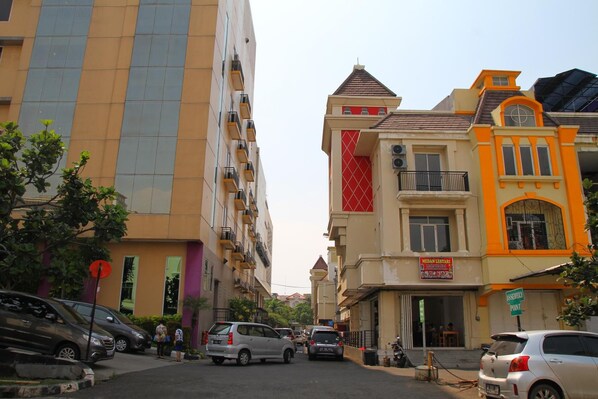 A street view with multi-story buildings, parked cars, and a few pedestrians.