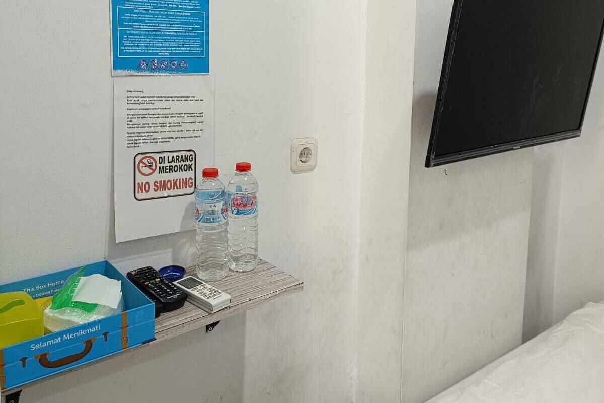Habitación de hotel con cama, televisor montado en la pared, estante con artículos de aseo y cartel de 'No fumar'.