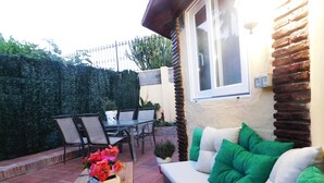Eine Terrasse im Freien mit einem Holztisch, einem weißen Sofa mit grünen Kissen sowie einem Essbereich mit Stühlen und einem Tisch.