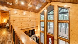 Ein Interieur einer Holzhütte mit Holzwänden, einer Treppe und großen Fenstern, die einen Blick ins Freie ermöglichen.