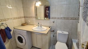 A bathroom with a washing machine, sink, toilet, and a mirror with a decorative border.