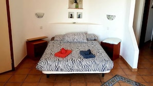 A single bed with a zebra print bedspread, two bedside tables, a nightstand, and a small rug on a tiled floor.