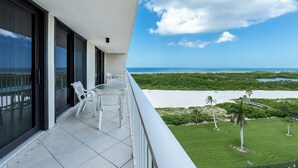 A balcony with a glass door, a small table with chairs, and a view of a beach and ocean. - South Seas Tower Two # 810.  Condo with Balcony, Beach, Pool and Fitness Facility. (Marco Island)