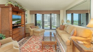 A spacious living room with a large flat-screen TV, a sofa, a coffee table, and a decorative cabinet.