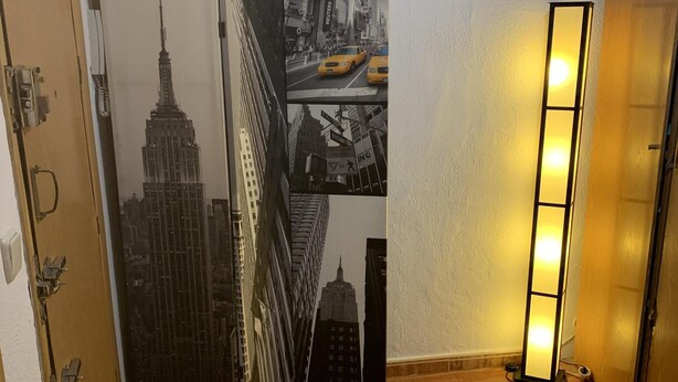A room with a wooden floor, a round cushioned area, a door with a cityscape artwork, and a standing lamp. - Apartment very close to Gran Via Sol WiFi Museums  (Madrid)