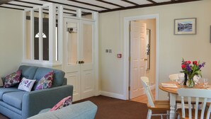 A room with a blue sofa, a dining table with chairs, and a door leading to another room. - 2 bedroom accommodation in Buckland Brewer, near Bideford (Buckland Brewer, near Bideford)