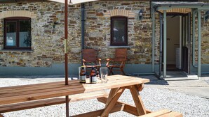 A stone building with a wooden table and chairs under a large umbrella, a door, and a window. - 2 bedroom accommodation in Buckland Brewer, near Bideford (Buckland Brewer, near Bideford)