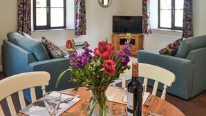 A living room with two sofas, a dining table with chairs, a TV, and a vase with flowers. - 2 bedroom accommodation in Buckland Brewer, near Bideford (Buckland Brewer, near Bideford)