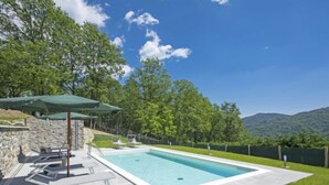 Une piscine rectangulaire avec un mur en pierre et une zone herbeuse.