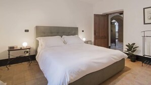 Une chambre avec un grand lit, des tables de chevet avec des lampes, une porte en bois et une plante en pot.