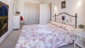 Une chambre à coucher avec un lit, une table de chevet, une commode, une porte et un mur orné d’un tableau.