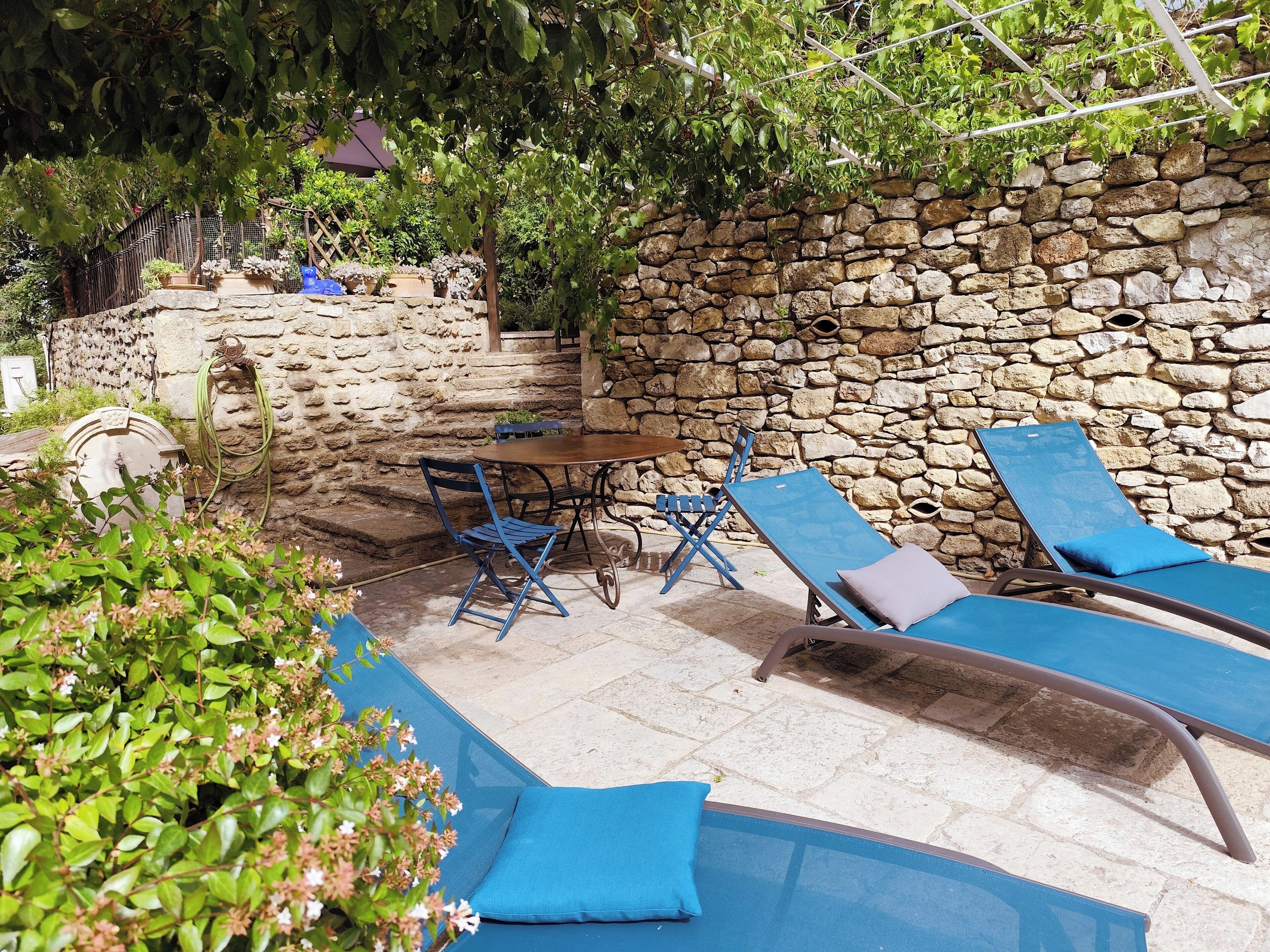 An outdoor patio with stone walls, a table with chairs, and blue lounge chairs.