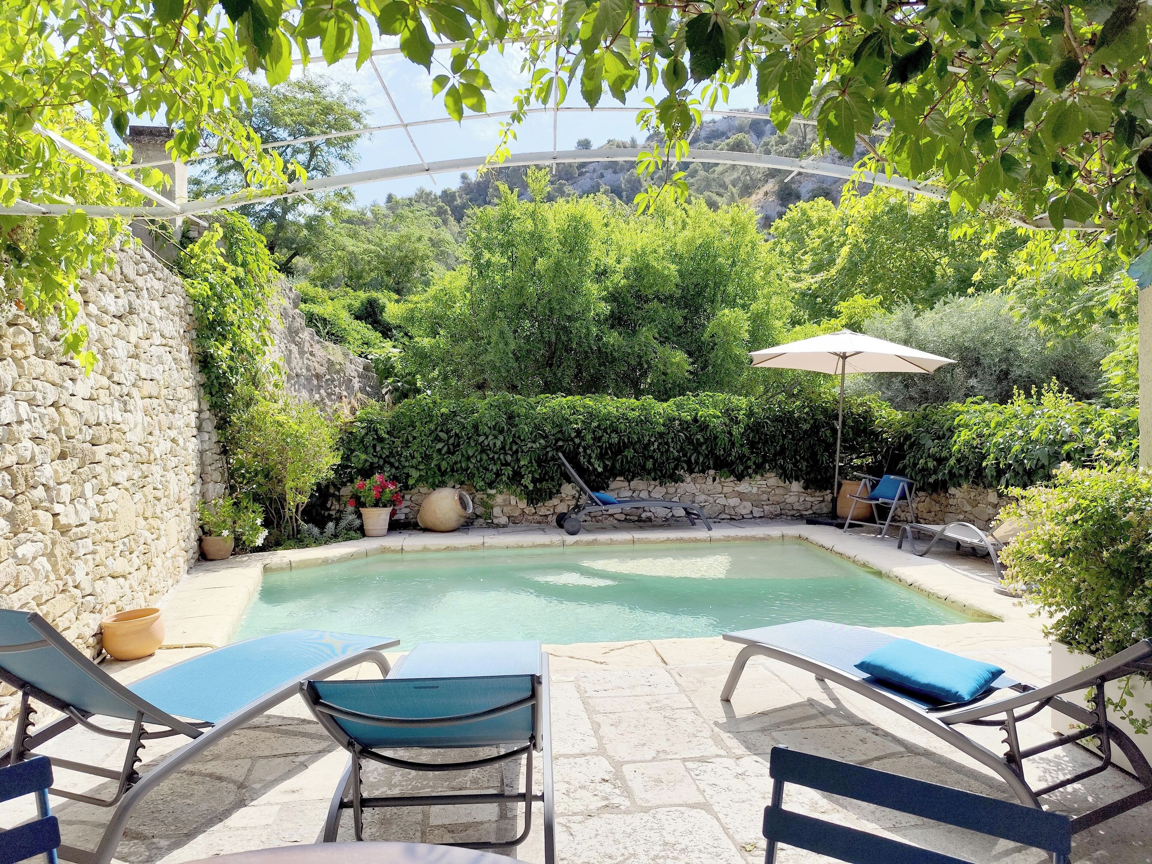 Area piscina con lettini e un tavolo, circondata da muri in pietra e vegetazione.