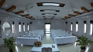 Ein Konferenzraum mit weißen Tischen und Stühlen, Deckenventilatoren und großen Fenstern.