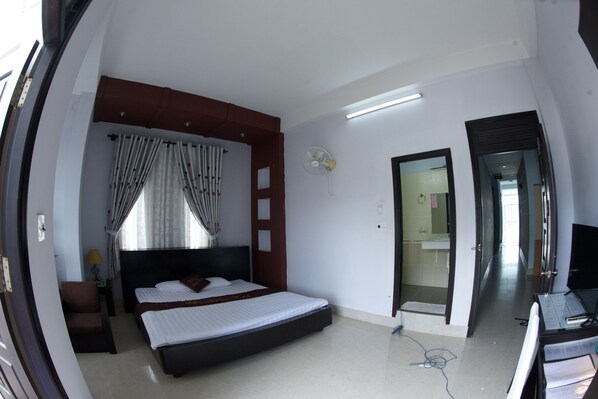 Una habitación de hotel con una cama, un escritorio, una silla, una ventana con cortinas, una puerta y un ventilador.
