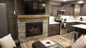 A modern kitchen with a stone fireplace, dark wooden cabinets, and stainless steel appliances. - Beautiful 3 Bed , 3 Bath with Great Location! Renovated in 2025!  (Boyne Falls)
