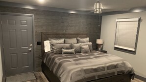 A bedroom with a bed, a nightstand, a lamp, a window with blinds, a door, and a ceiling fan. - Beautiful 3 Bed , 3 Bath with Great Location! Renovated in 2025!  (Boyne Falls)