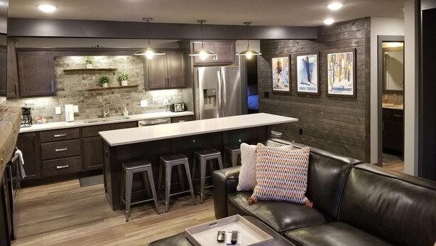 A modern kitchen with dark wood cabinets, a central island with stools, a refrigerator, and pendant lighting. - Beautiful 3 Bed , 3 Bath with Great Location! Renovated in 2025!  (Boyne Falls)