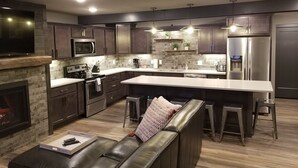 A modern kitchen with dark wood cabinets, stainless steel appliances, a large island, and a built-in fireplace. - Beautiful 3 Bed , 3 Bath with Great Location! Renovated in 2025!  (Boyne Falls)