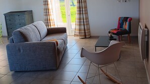 A living room with a sofa, a rocking chair, a television, and a sliding glass door to the outdoors. - GITE: Country house, near the landing beaches, with table football. (Le Molay-Littry)