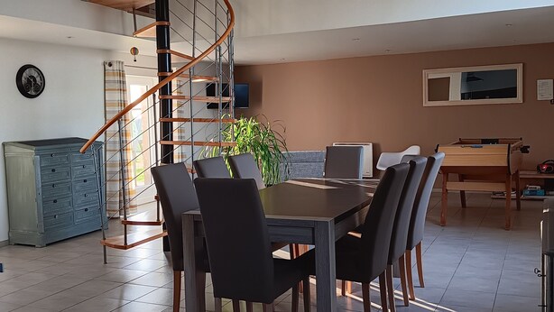A modern kitchen with a central island, a dining area with a wooden table and chairs, and a spiral staircase leading to an upper level. - GITE: Country house, near the landing beaches, with table football. (Le Molay-Littry)