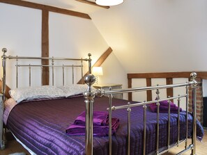Un lit avec un cadre en métal, un oreiller blanc et une couverture violette.