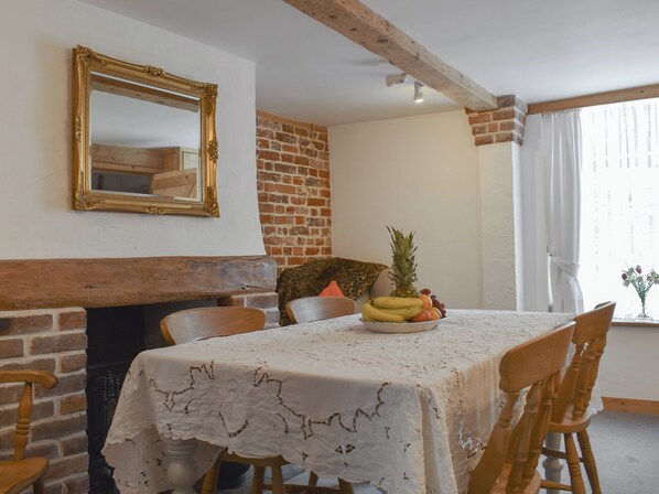 Ein Essbereich mit einem mit Spitze bedeckten Tisch, einer Obstschale, einem Spiegel und einem Kamin aus Backsteinen.
