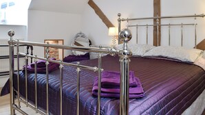 Une chambre à coucher avec un lit en métal, une couvre-lit violette et une poutre en bois au plafond.