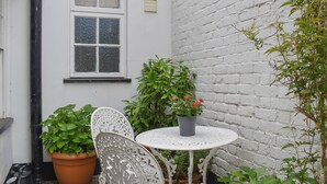 Un bâtiment en briques blanches avec une fenêtre, une table blanche sur laquelle est posée une plante en pot et une chaise blanche.