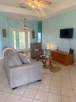 A living room with a grey sofa, a wooden sideboard, a television, and a ceiling fan.