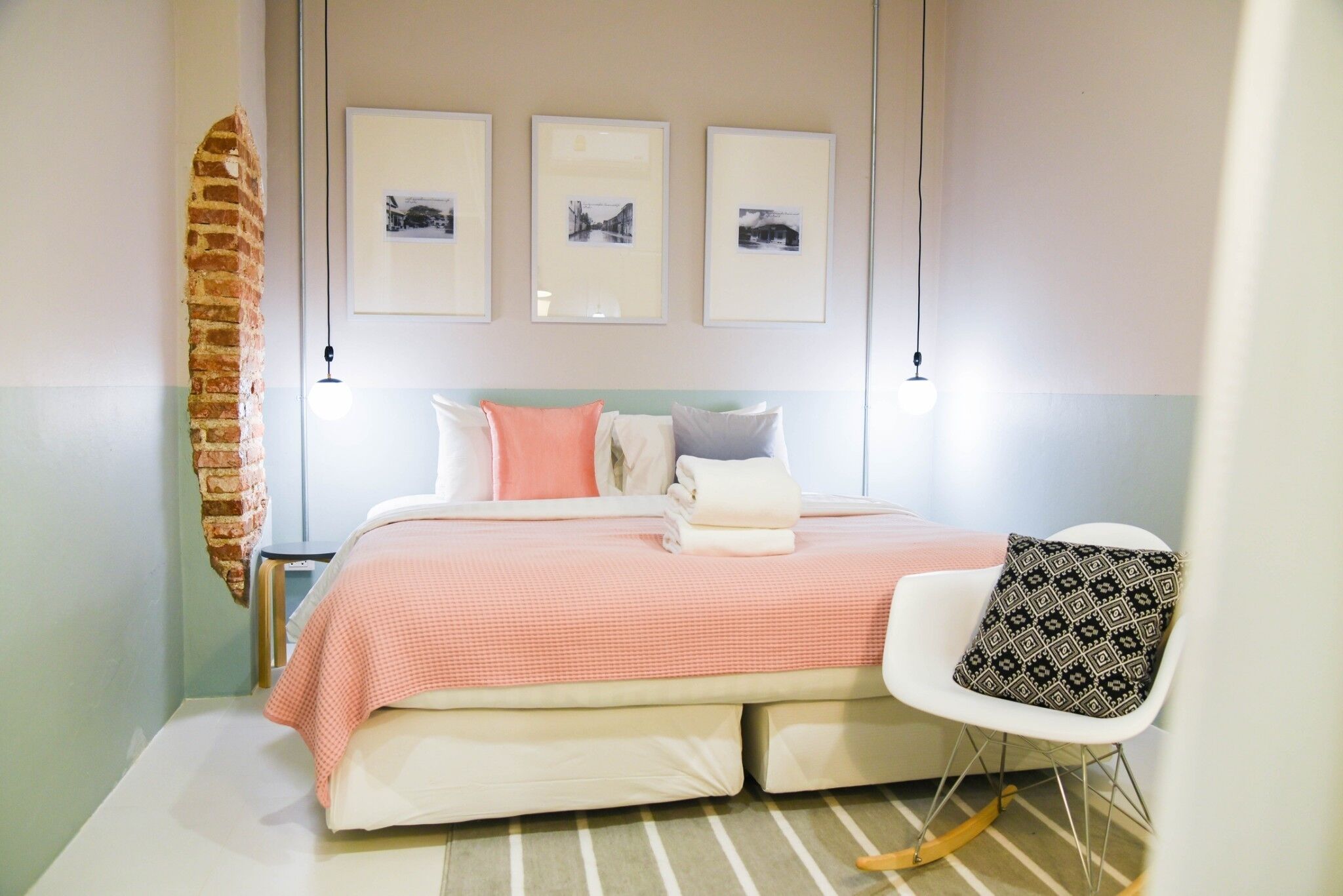 Ein ordentlich eingerichtetes Schlafzimmer mit einem Bett, Kissen, einem Sessel und gerahmten Bildern an der Wand.