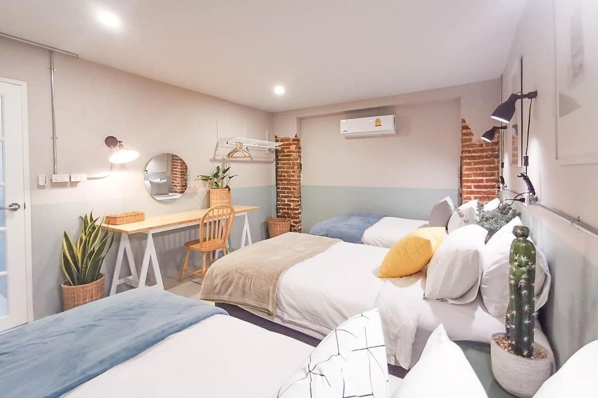 A bedroom with a bed, a desk, a chair, a potted plant, and a wall-mounted air conditioner.