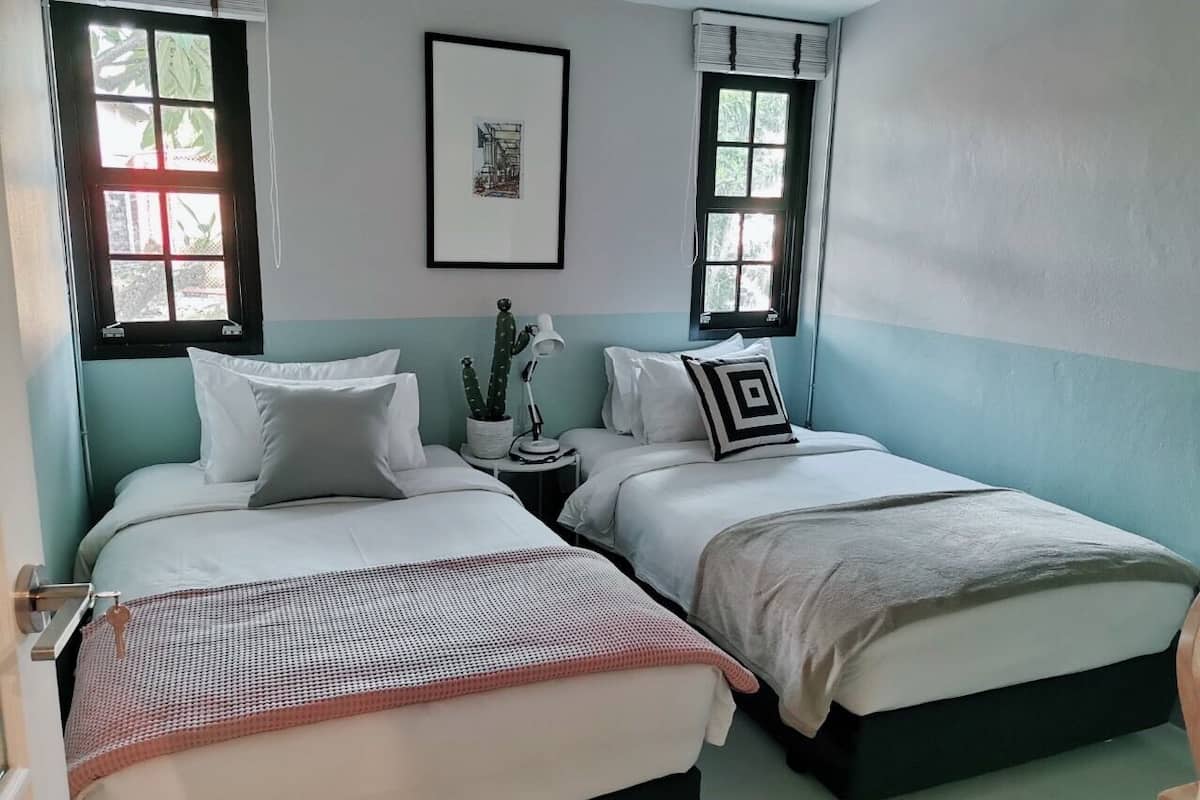 A room with two beds, a small table with a lamp, and a framed picture on the wall.
