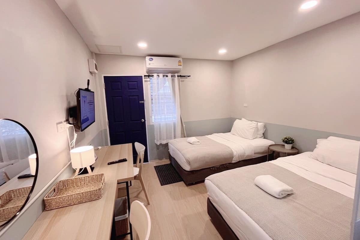 A compact hotel room with a single bed, a desk with a chair, a small table, a TV mounted on the wall, and a window with curtains.