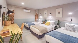 A hotel room with three beds, a wooden table, and a brick accent wall. - Snoozy (Phuket)