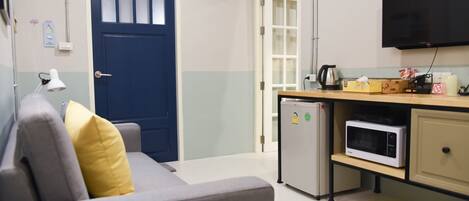 A compact room with a sofa, a microwave, a small refrigerator, a television, and a door with frosted glass panels.