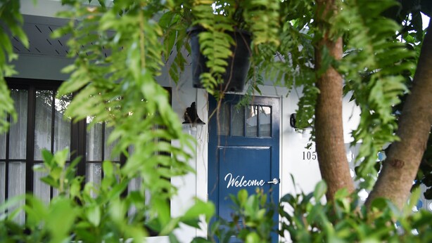 A building with a blue door marked "Welcome" and a number "105" on the wall. - Snoozy (Phuket)
