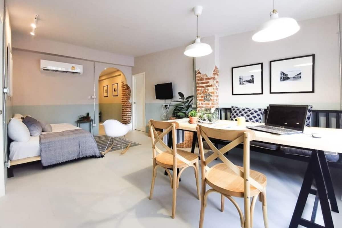 A modern living room with a sofa, a dining table with chairs, a laptop, and a brick wall.