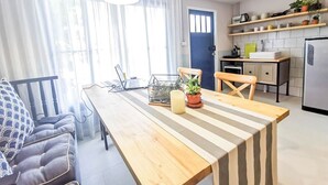 A modern kitchen with a wooden island, a dining area with a striped tablecloth, and a blue door. - Snoozy (Phuket)