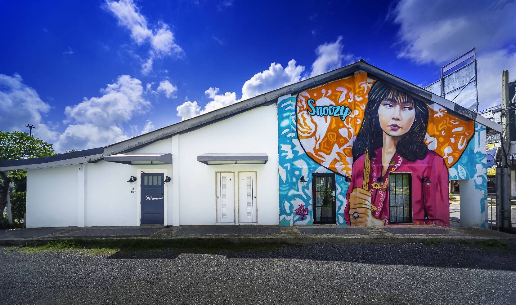 Un edificio con un murale raffigurante una donna che tiene un coltello, una porta blu e un cartello con su scritto 'Welcome'.