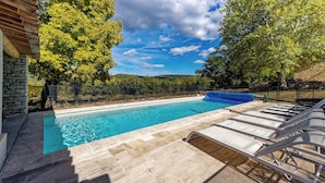 A swimming pool with clear blue water, surrounded by stone walls and lounge chairs. - Homerez - Villa in Saignon (Saignon)