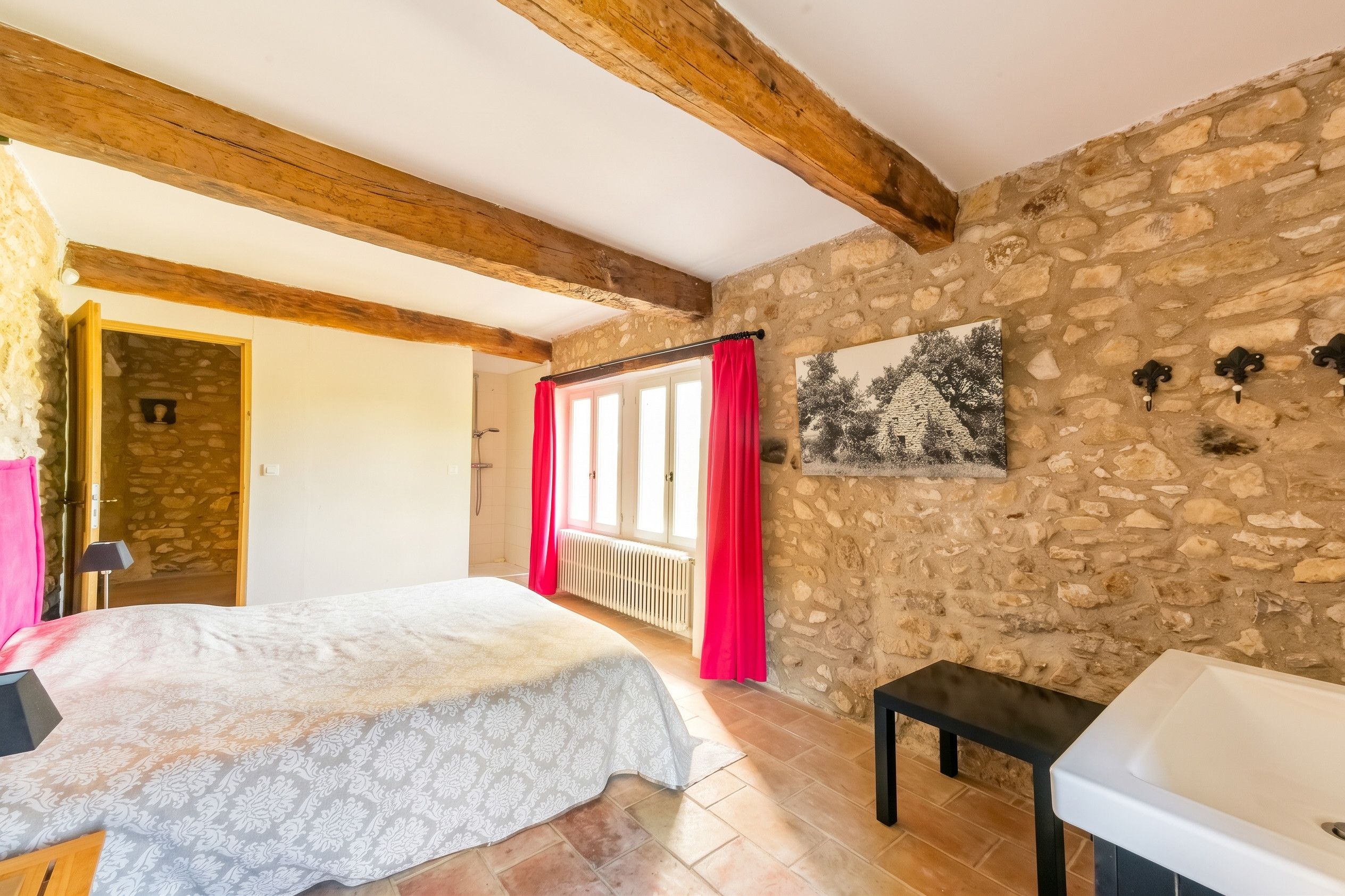 Ein Schlafzimmer mit einer Steinwand, einem Bett mit gemustertem Überwurf, einem roten Vorhang, einer schwarzen Bank und einem weißen Waschbecken.