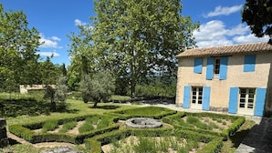 A traditional stone building with blue shutters, surrounded by a well-maintained garden with hedges and a central circular stone feature. - Homerez - Villa in Saignon (Saignon)